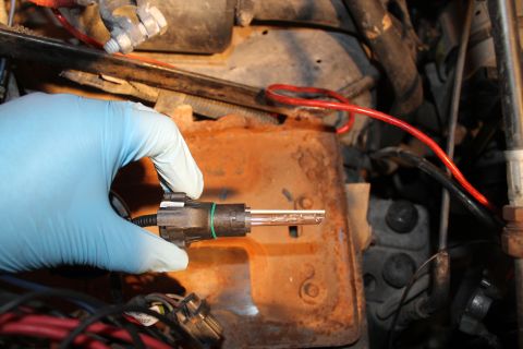 1990 Ford Bronco - Close-up of a hand holding a vehicle sensor with a green O-ring, with engine components in the background.