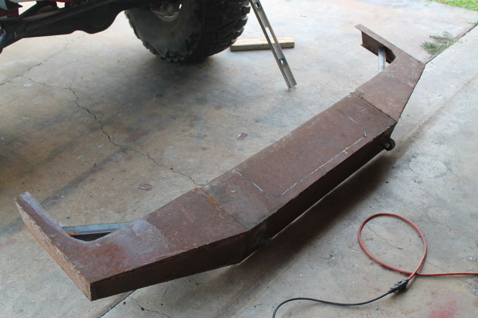 Custom fabricated steel bumper, rusty, with angled ends and a central section marked for cuts