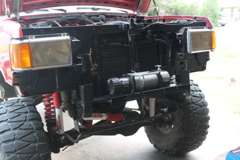 1990 Ford Bronco - Front view of a red Ford truck with a winch installed, showing large tires and suspension modifications.
