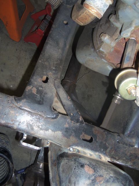 1968 Ford Bronco - Close-up view of a rusty vehicle frame and suspension components, with jack stands in the background.