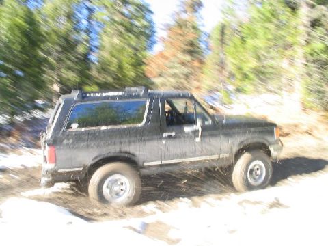 1988 Ford Bronco - Black 1988 Ford Bronco navigating a snowy, muddy trail with trees in the background.
