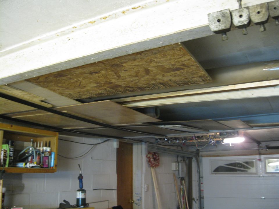 Garage interior with exposed ceiling joists, plywood sheeting, and a closed garage door