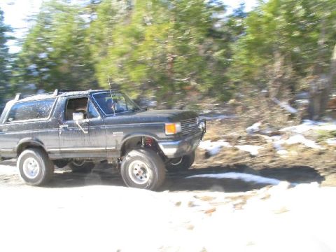 1988 Ford Bronco - This Ford Bronco is navigating a wooded area with patches of snow on the ground.