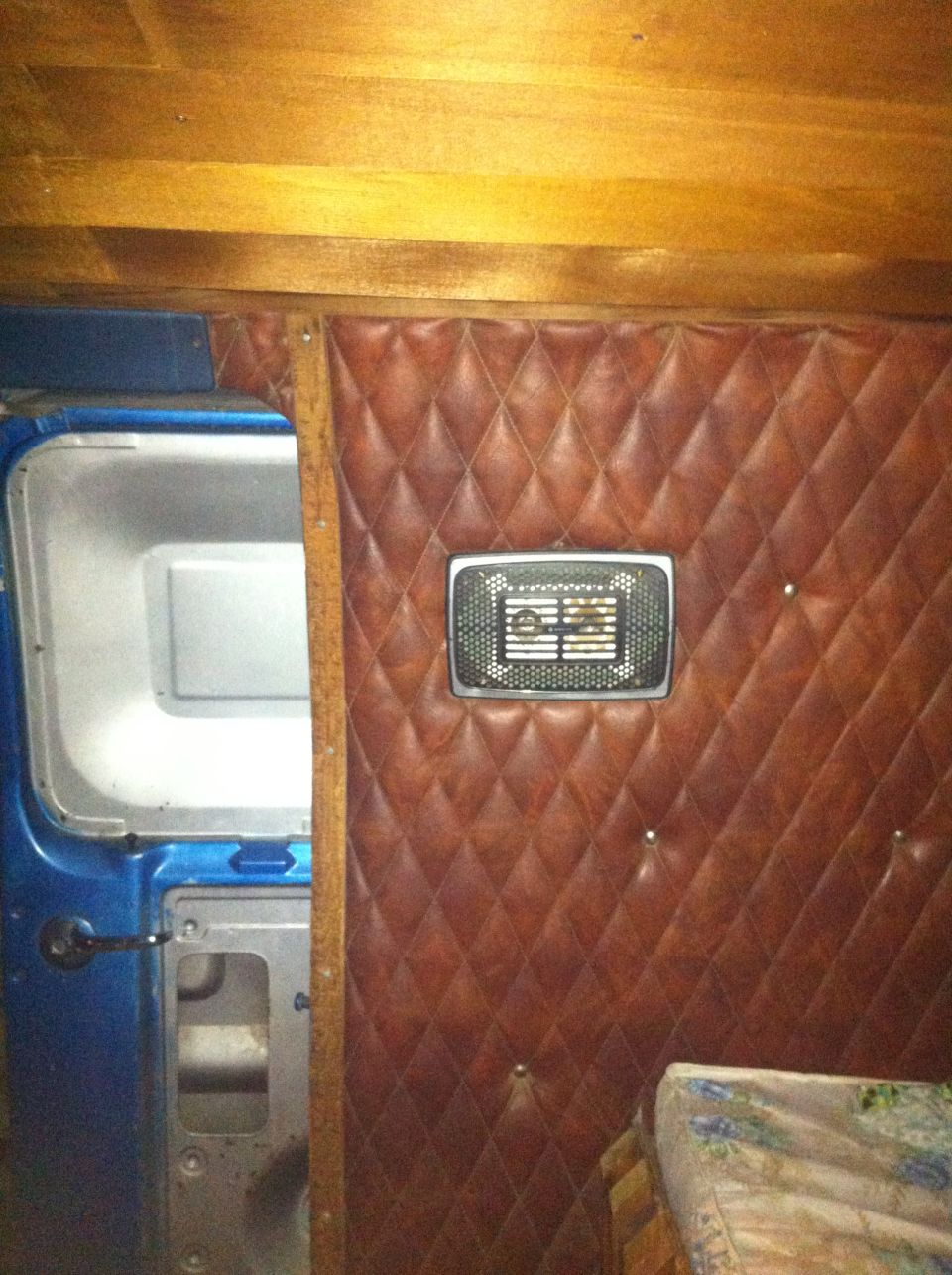 Quilted brown upholstery on the interior wall of a van, with a vent and a blue door frame visible