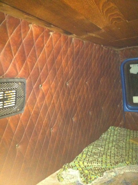 1977 Ford E350 - The interior of a van features diamond-tufted brown upholstery and wood paneling, with a glimpse of a blue window frame.