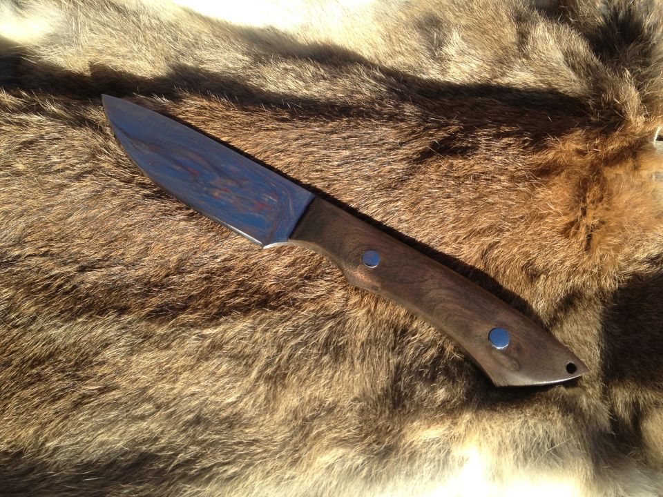 Knife with wooden handle and metallic blade rests on a furry surface