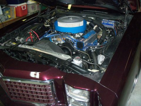1979 Ford Ranchero - Open engine bay of a dark maroon/burgundy car photographed from the front corner in a garage, showing a Ford V8 with blue-painted valve cov…