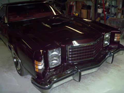 1979 Ford Ranchero - High three-quarter front view of a freshly painted deep burgundy Ford Ranchero in a garage, with a script "Ranchero" hood emblem, hood scoo…