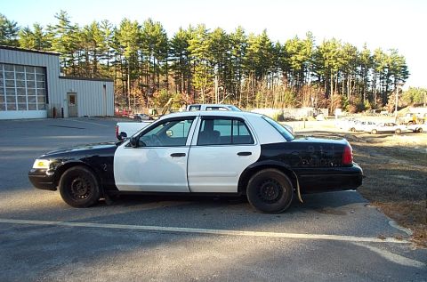 2001 Ford Crown Victoria - A black and white police car is parked outside a building with trees in the background.