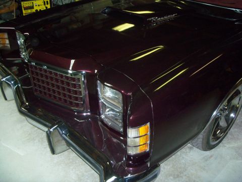 1979 Ford Ranchero - Tight high-angle shot of the passenger-side front corner of a glossy deep burgundy Ford Ranchero in a garage, showing the chrome-trimmed eg…
