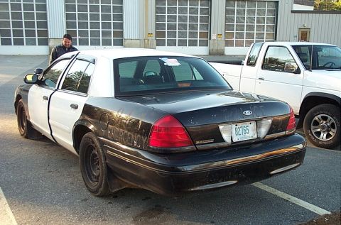 2001 Ford Crown Victoria - A black and white 2001 Ford Crown Victoria police car is parked next to a white pickup truck.