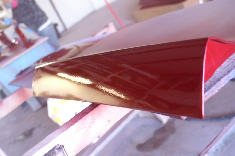 Red car part with glossy finish, angled view, resting on wood
