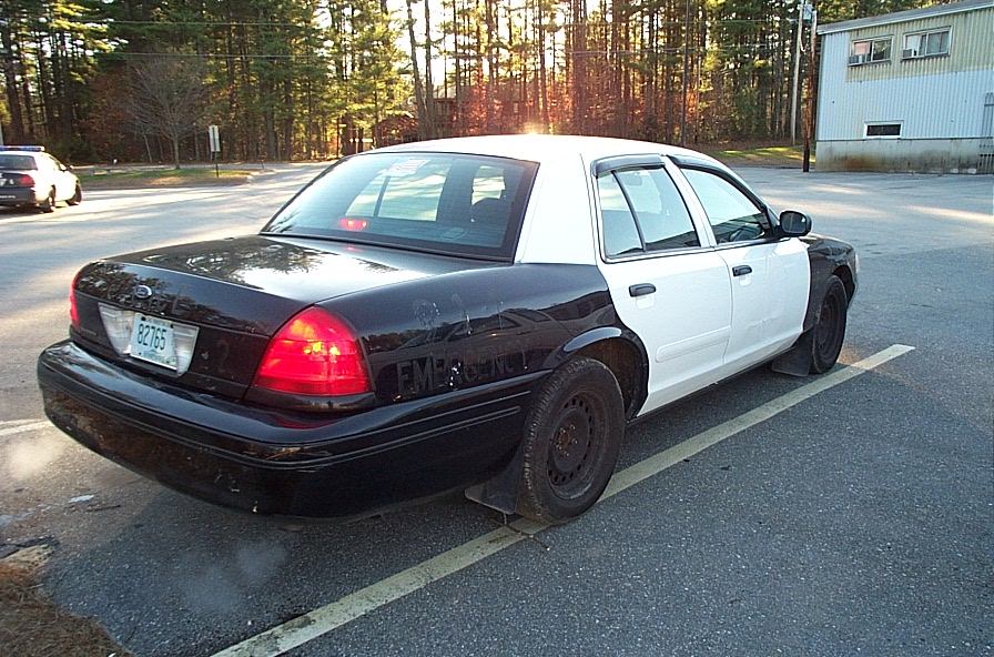 Black and white police car parked, another police car in background. License plate 82765