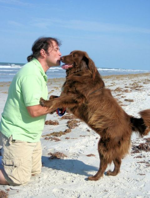1976 Ford Ranchero - A man kneels on the sand to kiss a large brown dog on a beach, with the ocean waves visible behind them.