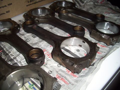 1995 Ford Probe - Several engine connecting rods are laid out on a surface covered with newspaper that displays pricing information.