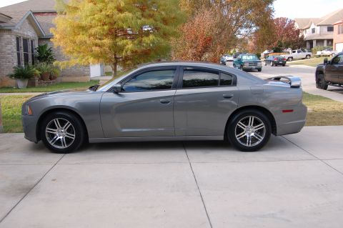 2012 Dodge Charger - A gray sedan with a spoiler is parked on a driveway, with other vehicles and houses in the background.