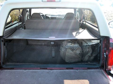1994 Ford Bronco - Rear cargo area of a full-size SUV shot straight in through the open tailgate with the rear glass raised, showing a gray retractable cargo…