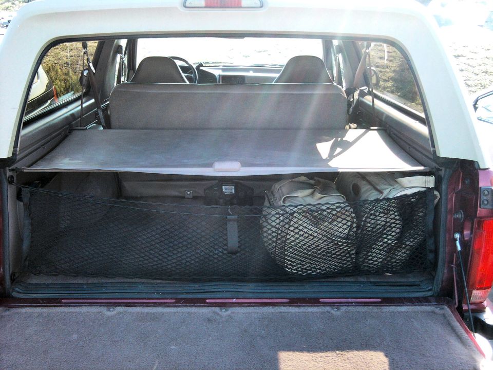 SUV rear cargo area with gray cargo cover and black cargo net holding a tan duffel bag