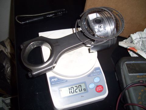 1995 Ford Probe - A connecting rod and piston assembly is weighed on a digital scale, showing a reading of 1020 grams.