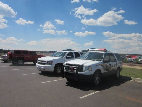 1991 Ford LTD Crown Victoria - Several vehicles, including a Sheriff's SUV, are parked in a lot under a blue sky with clouds.