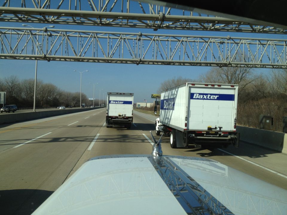 Two white semi-trucks with 'Baxter' branding driving on a highway under an overpass