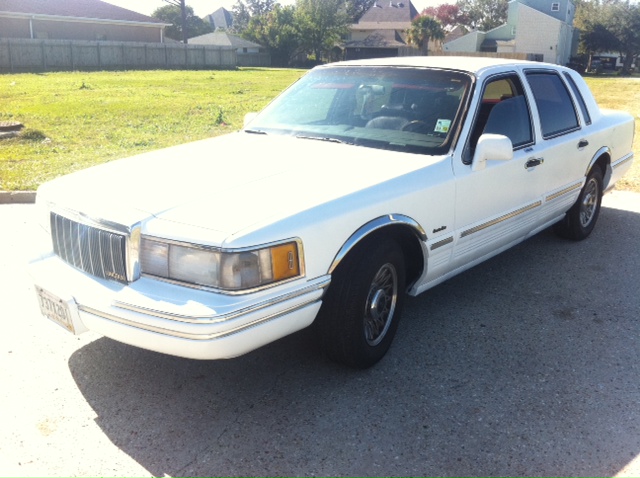 White 1997 Lincoln Town Car parked on asphalt with grass and houses in background