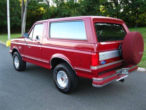 1994 Ford Bronco - Rear view of a red 1994 Ford Bronco parked on asphalt with trees in the background.