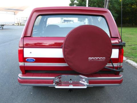 1994 Ford Bronco - The rear of a red Ford Bronco is shown, a spare tire cover and a white stripe along the side.