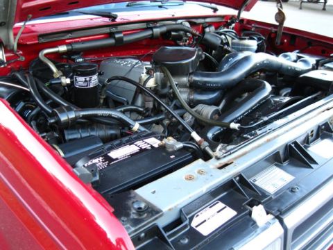 1994 Ford Bronco - The engine bay of a red vehicle, showing the battery, hoses, and engine components.