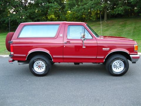 1994 Ford Bronco - Side profile of a red 1994 Ford Bronco SUV with a spare tire on the back.