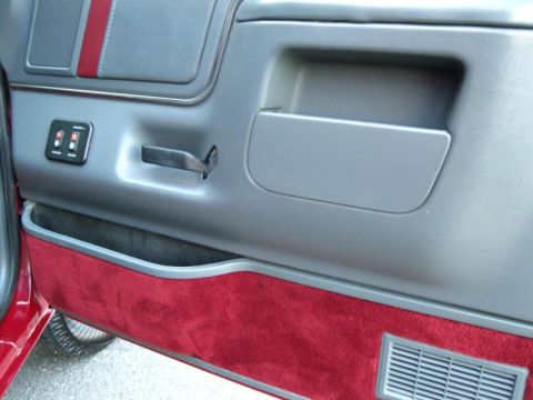 1994 Ford Bronco - Close-up of a car's interior door panel, showing red carpet and gray plastic accents.