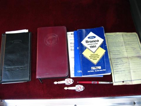 1994 Ford Bronco - Ford Bronco owner's manual and keys are laid out on a dark red surface.