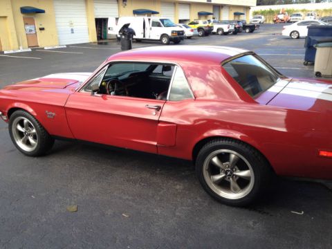 1968 Ford Mustang - A red 1968 Ford Mustang coupe is parked in a lot, showing off its classic lines and white racing stripes.