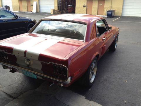1968 Ford Mustang - A red 1968 Ford Mustang with white racing stripes is parked in an outdoor lot.