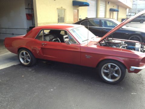 1968 Ford Mustang - A red 1968 Ford Mustang coupe is parked with its hood open, revealing the engine bay.
