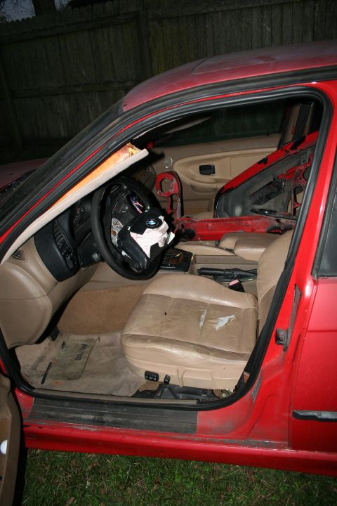 1996 BMW 3 Series - The interior of a red BMW shows damage to the driver's seat and the passenger side door panel is removed.