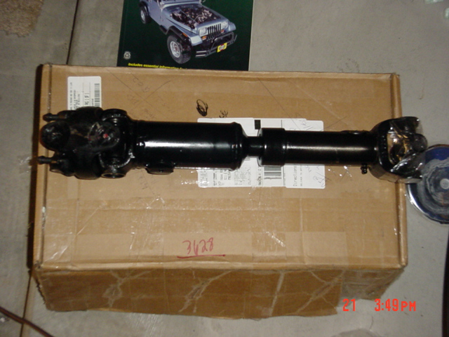 Driveshaft with U-joints lying on a cardboard box, Jeep parts catalog behind it