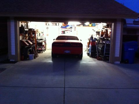 2010 Dodge Challenger - A red Dodge Challenger is parked inside a well-lit garage, with various items stored on shelves.