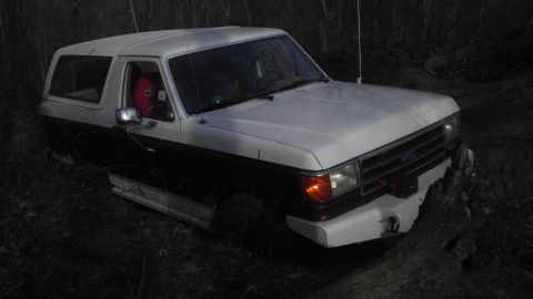 1989 Ford Bronco - This two-tone Ford Bronco is partially submerged in mud and appears to be stuck in a wooded area.