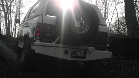 1989 Ford Bronco - Rear view of a 1989 Ford Bronco parked on an incline with a spare tire on the back.