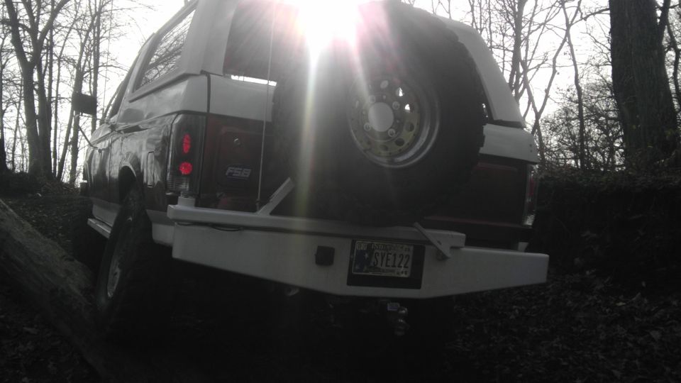 1989 Ford Bronco rear view with spare tire mounted on the tailgate, off-road bumper, and trees in background