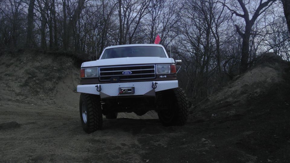 White Ford pickup truck with custom bumper and 4x4 badging, parked on a dirt incline