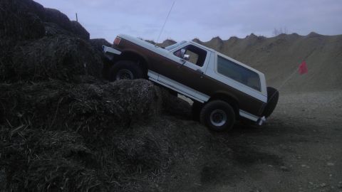 1989 Ford Bronco - A two-tone Ford Bronco navigates a steep incline of loose dirt and debris.