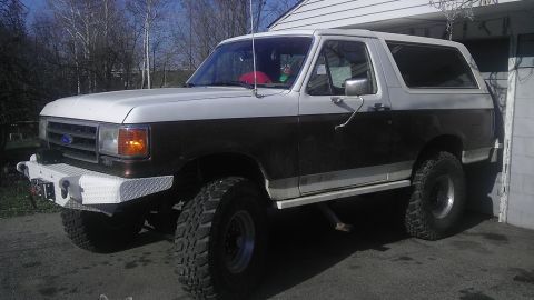 1989 Ford Bronco - This lifted Ford Bronco has a two-tone paint scheme and is parked in a driveway next to a building.