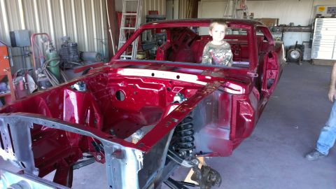 1970 Ford Mustang - Red 1970 Ford Mustang body undergoing restoration in a workshop, with a child in the driver's seat.