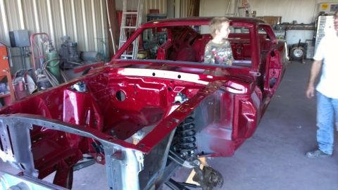 1970 Ford Mustang - A classic car body, possibly a 1969 Mustang, is being worked on in a garage, with a child sitting inside.
