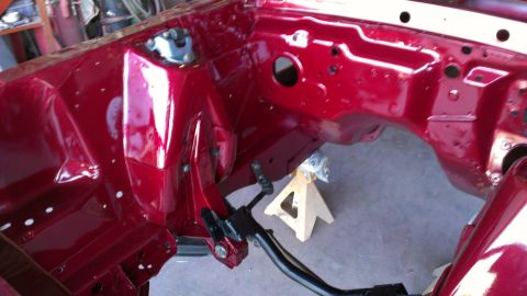 1970 Ford Mustang - The bare, red-painted engine bay frame of a vehicle is shown, supported by a jack stand.
