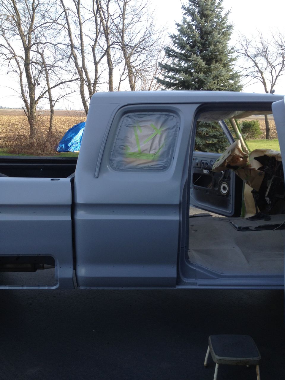Gray 1979 Ford F-350 pickup truck, side view, primer finish, driver's door open, interior covered