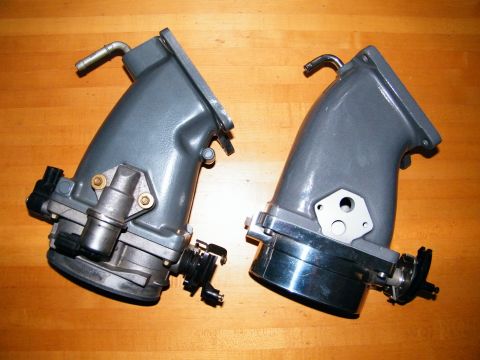2004 Ford Crown Victoria - Two throttle bodies are shown side-by-side on a wooden surface.