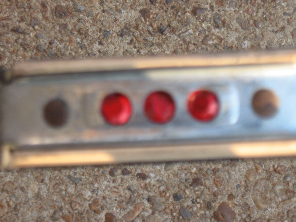 Metal strip with three red circular lights and two dark circular indentations